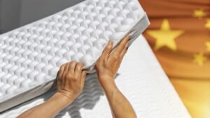 Close-up of hands adjusting a white textured mattress with a background of a blurred Chinese flag.
