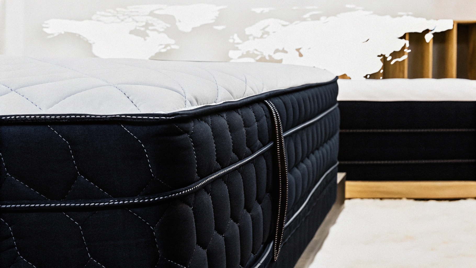 Close-up of a black quilted mattress with zipper detail, world map decor in the background.