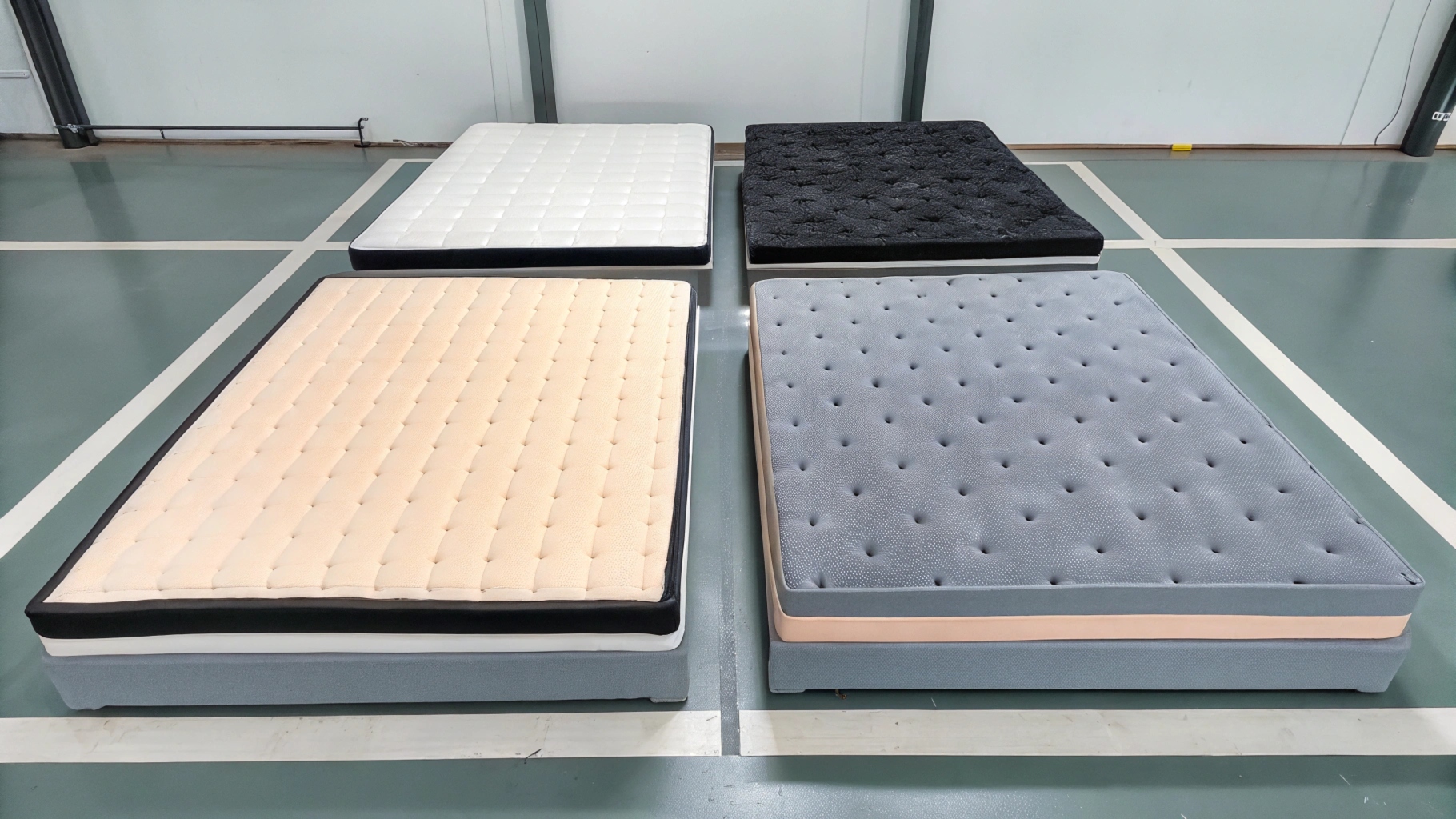 Four mattresses in different colors and designs displayed on a showroom floor.