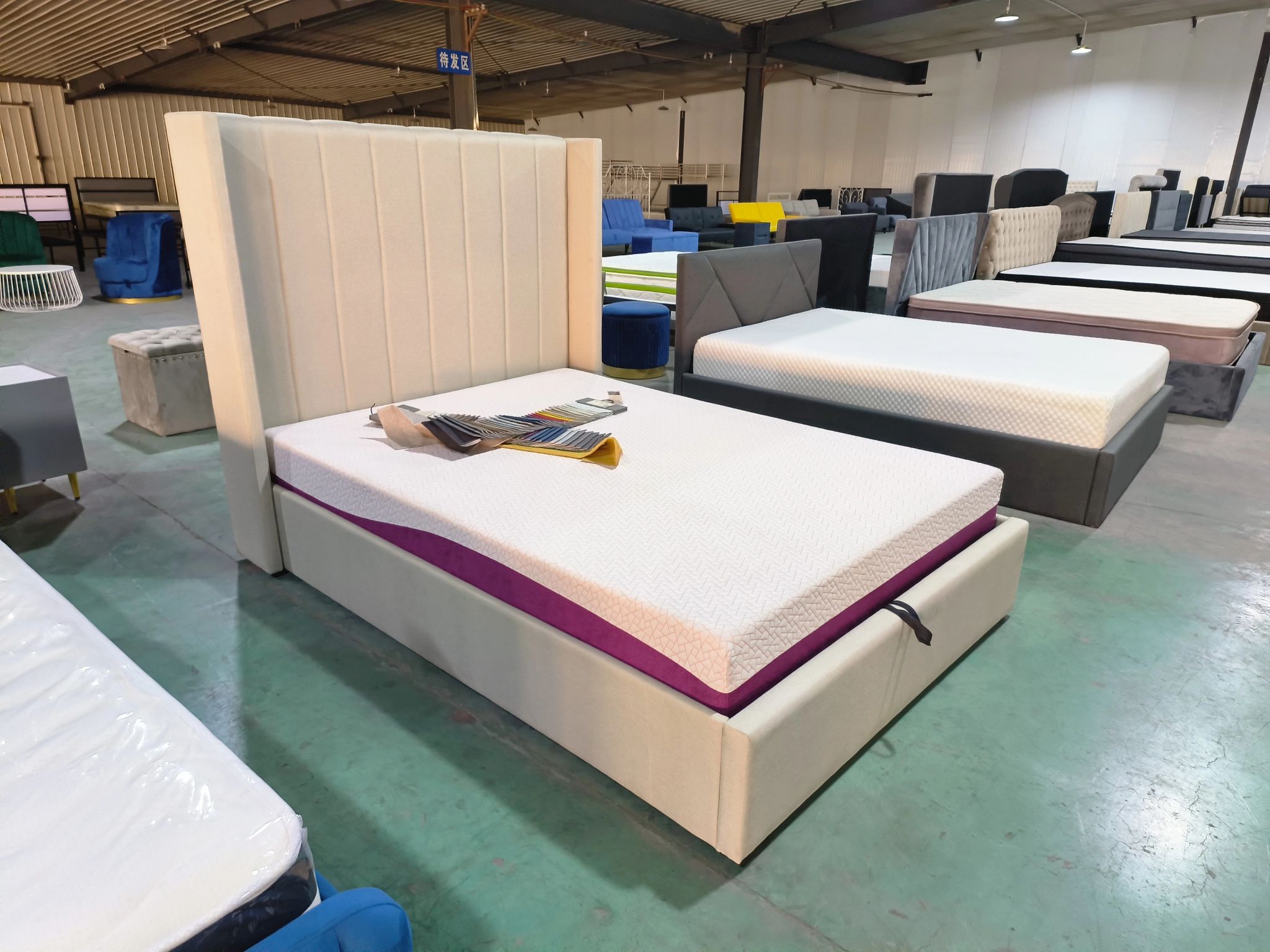 Beige upholstered bed frame with vertical panel headboard, memory foam mattress, and velvet color swatches displayed in a showroom.