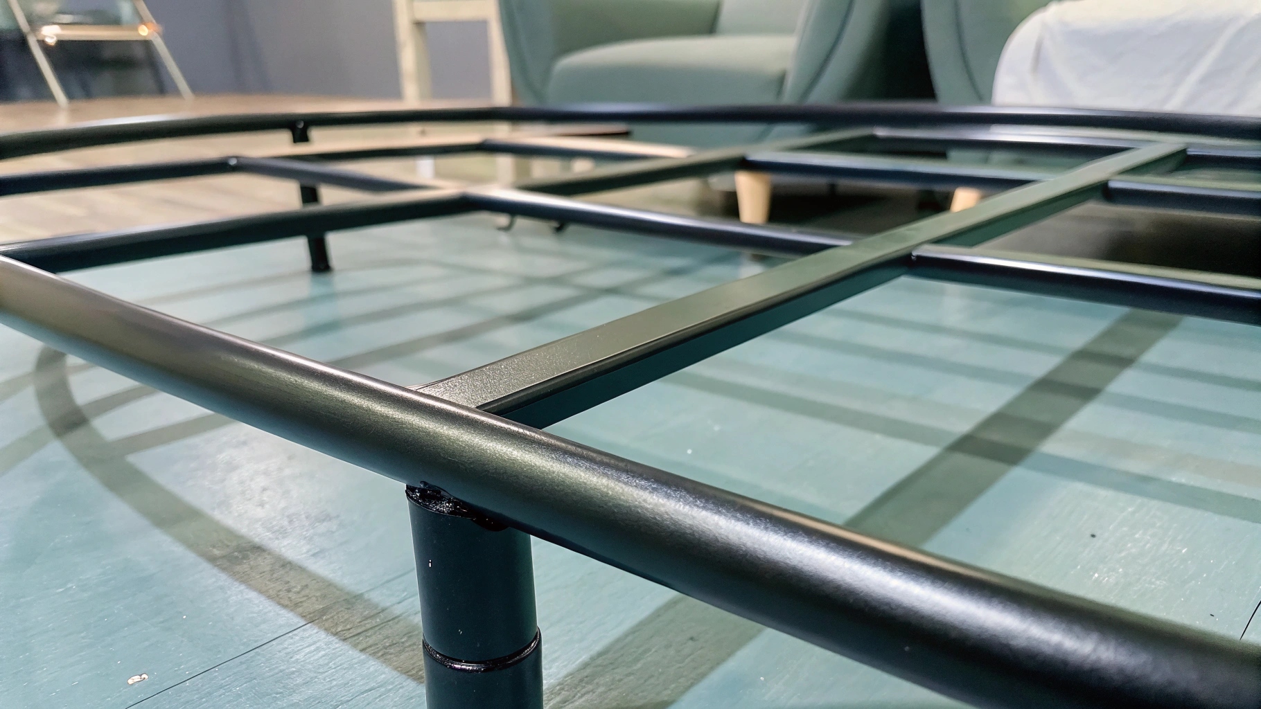 Close-up of a black metal bed frame on a blue wooden floor.