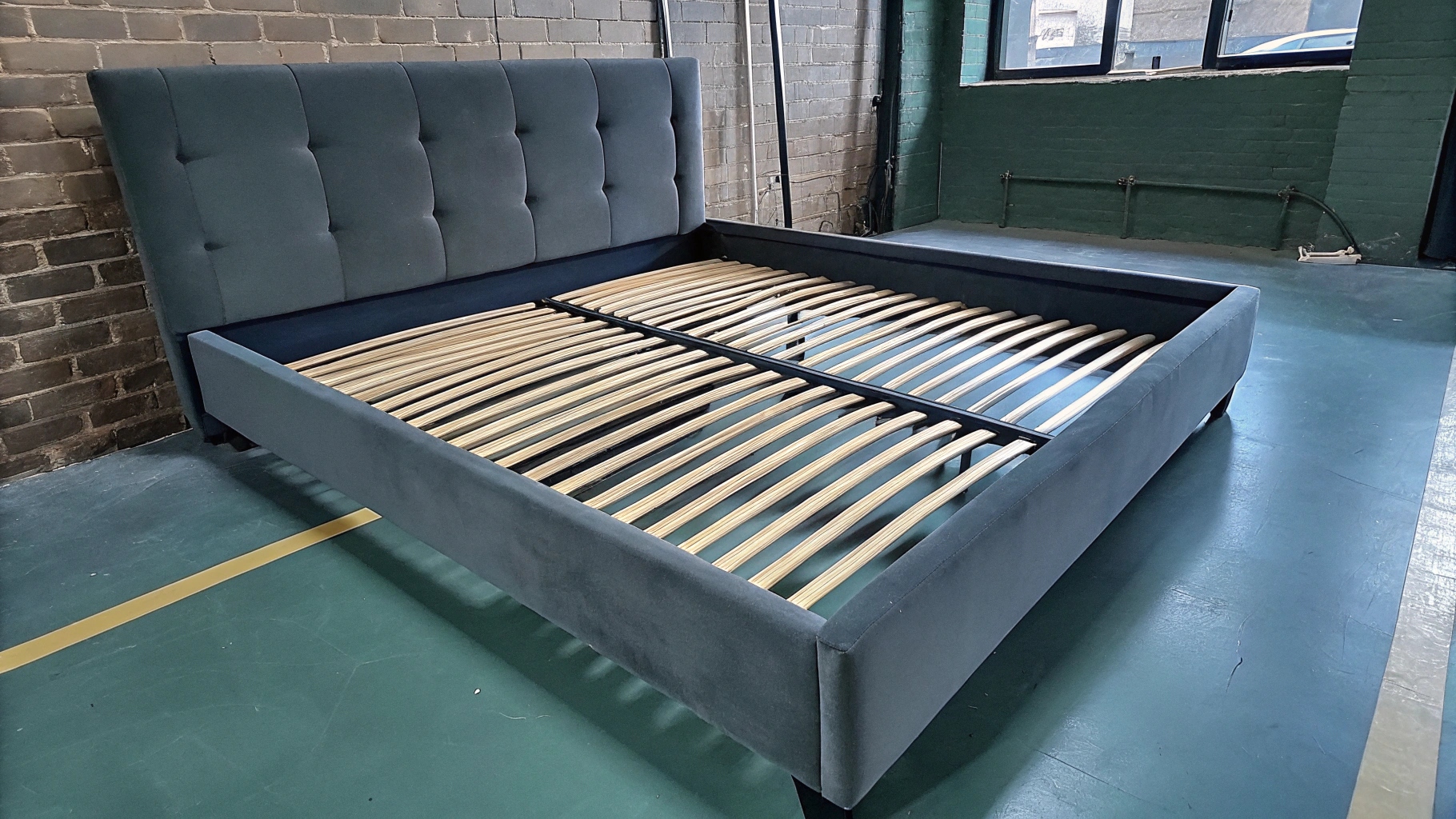 Modern upholstered bed frame with wooden slats in an industrial setting.