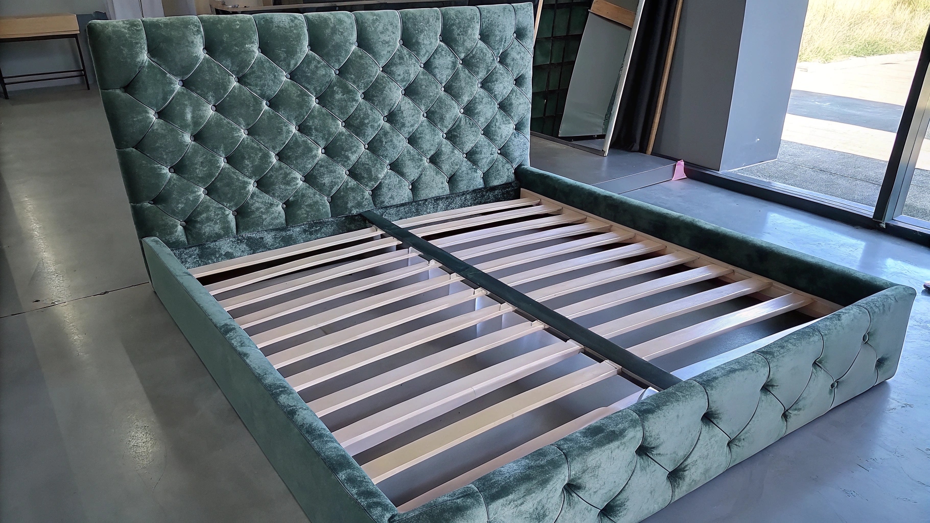 Elegant green velvet bed frame with tufted headboard and wooden slats.