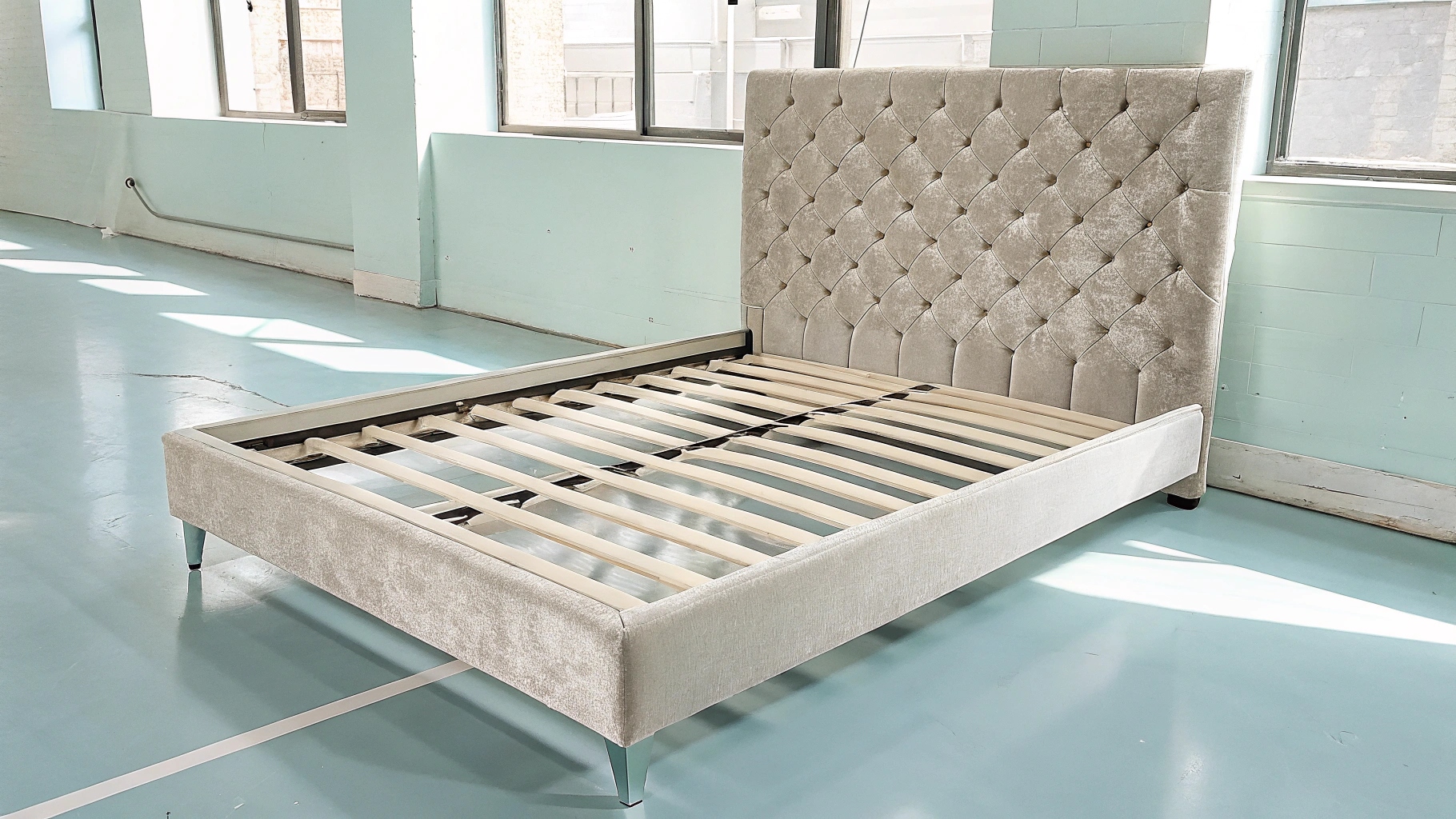 Beige velvet upholstered bed frame with tufted headboard, wooden slats, and sleek metal legs in a bright room.