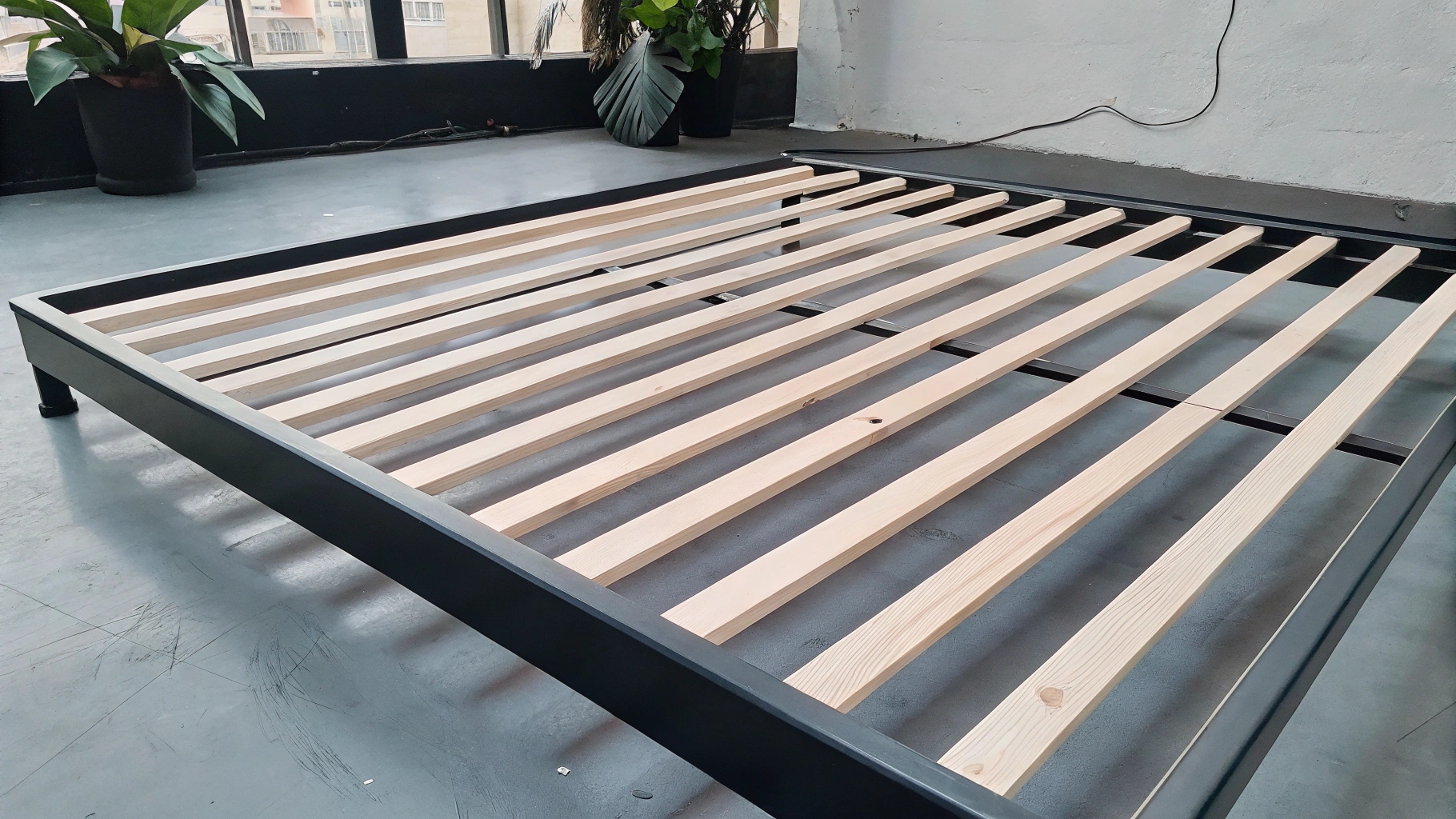 Wooden slatted bed frame with black metal edges in a modern room.