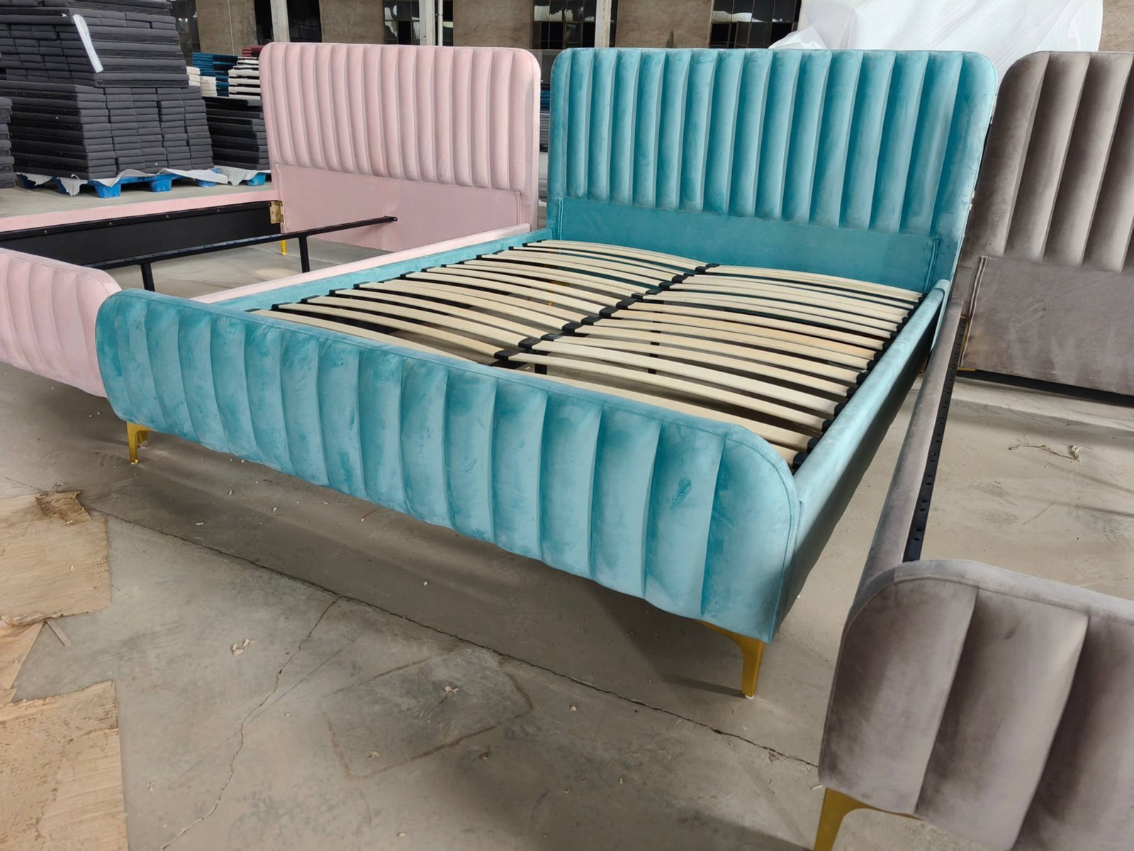 A stack of upholstered bed headboards in a factory, showing different velvet textures