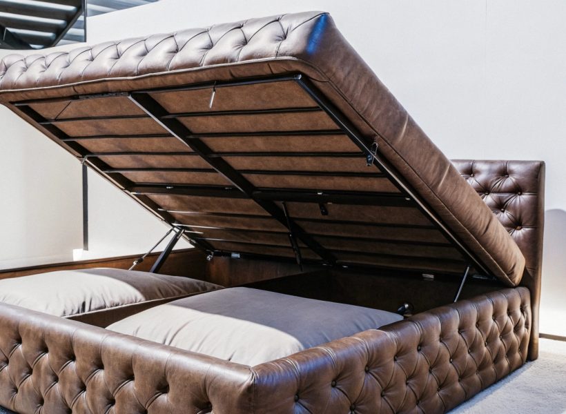 Brown leather upholstered bed with open storage compartment and padded headboard.